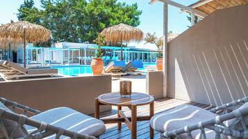 Zona junto a la piscina con sillones de descanso, una mesa de madera y vistas a la piscina y árboles.
