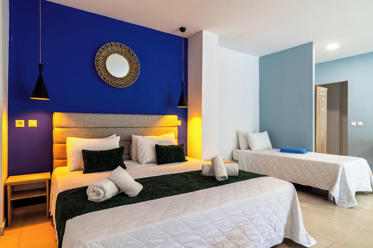 Habitación de hotel con dos camas, cabeceras, lámparas de noche, un espejo y una puerta.