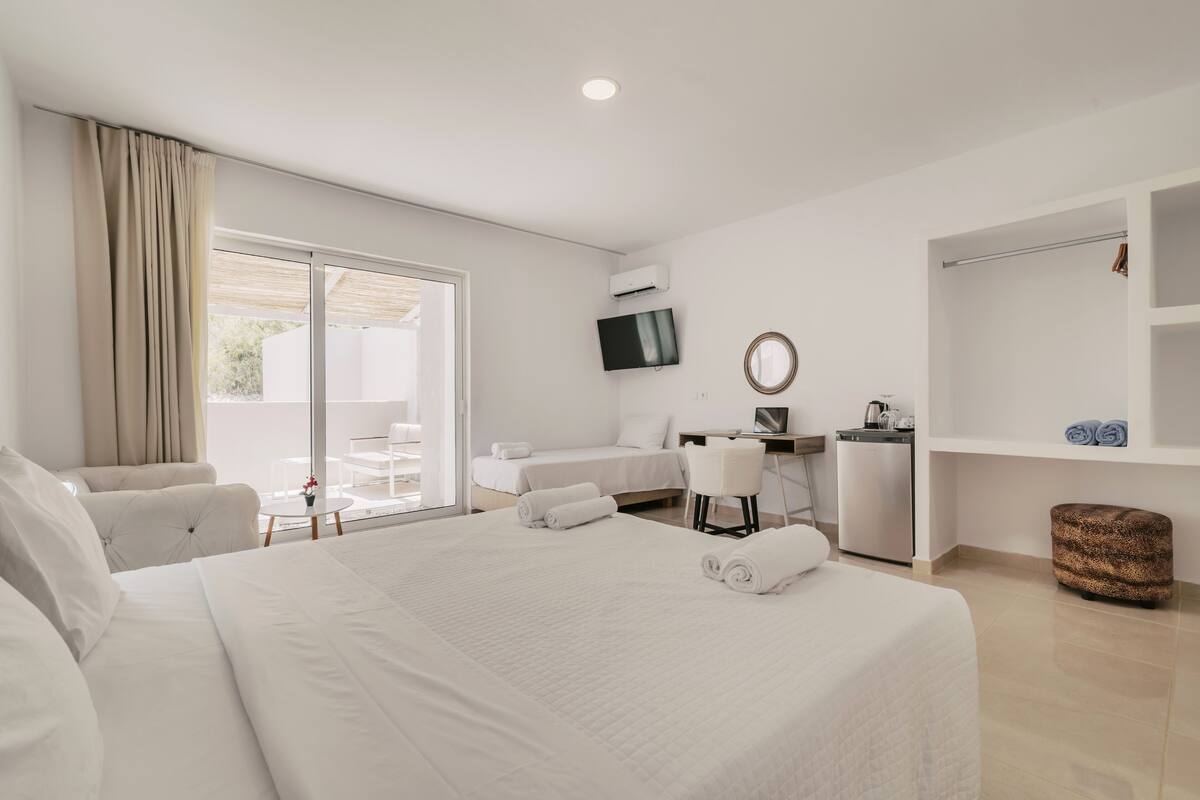 Habitación de hotel con una cama grande, un escritorio, una silla, un televisor y un balcón con vistas.