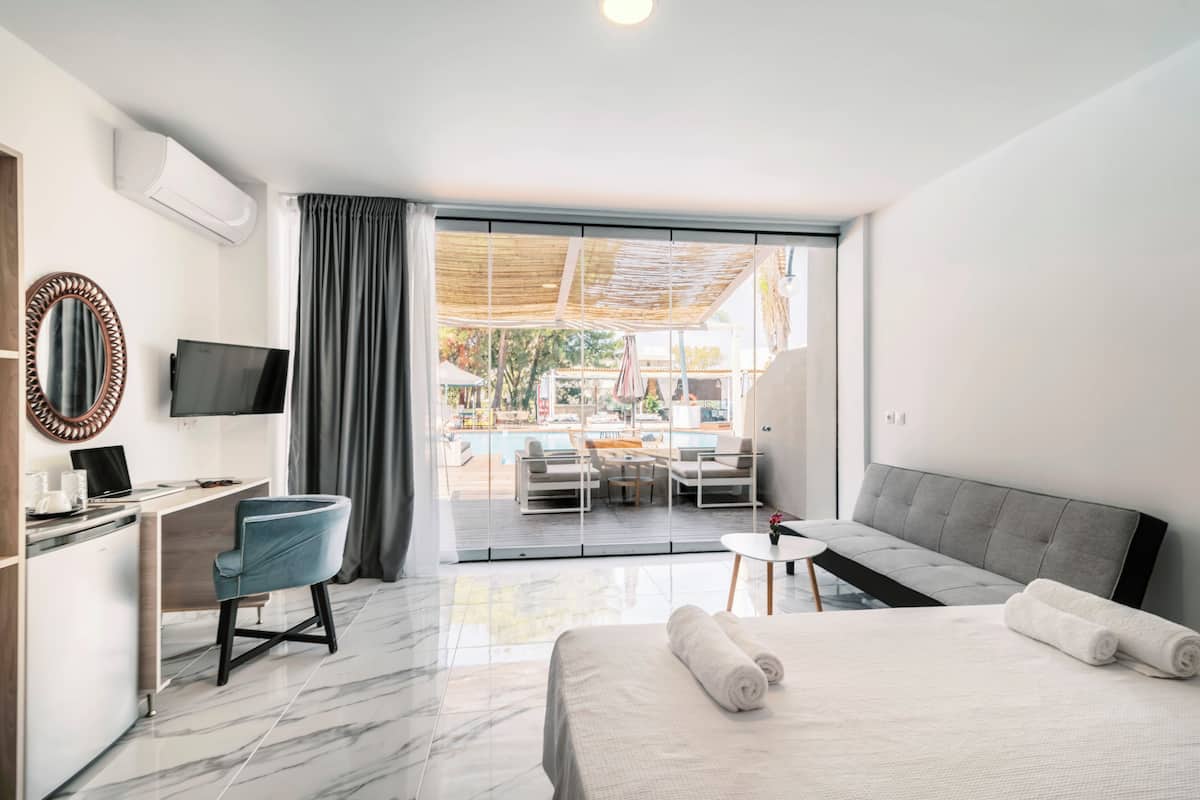 Habitación de hotel moderna con cama, escritorio, televisión y vistas a un área de piscina al aire libre.