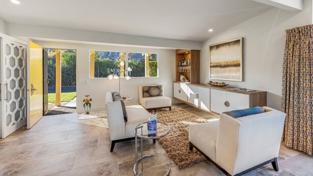 A spacious living area with a sofa, a coffee table, and a dining table. There is a large window providing a view of the outdoors. - Mid-Century Beauty! Community Pool! Hiking! Mountain Views! Walk to El Paseo! (Palm Desert)