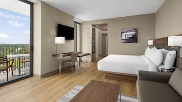 Habitación de hotel con cama, escritorio, silla, televisor y balcón con vista a la ciudad.