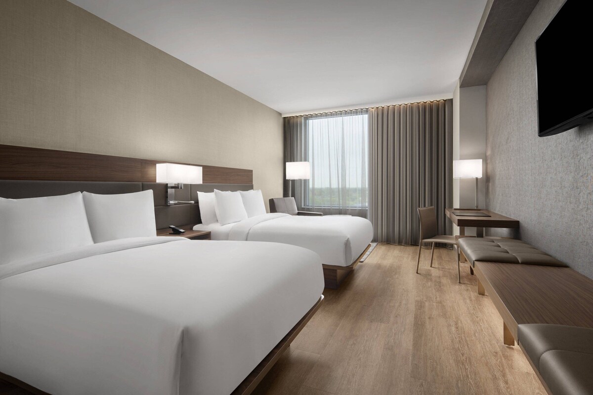 A hotel room with two beds, a desk, and a TV.