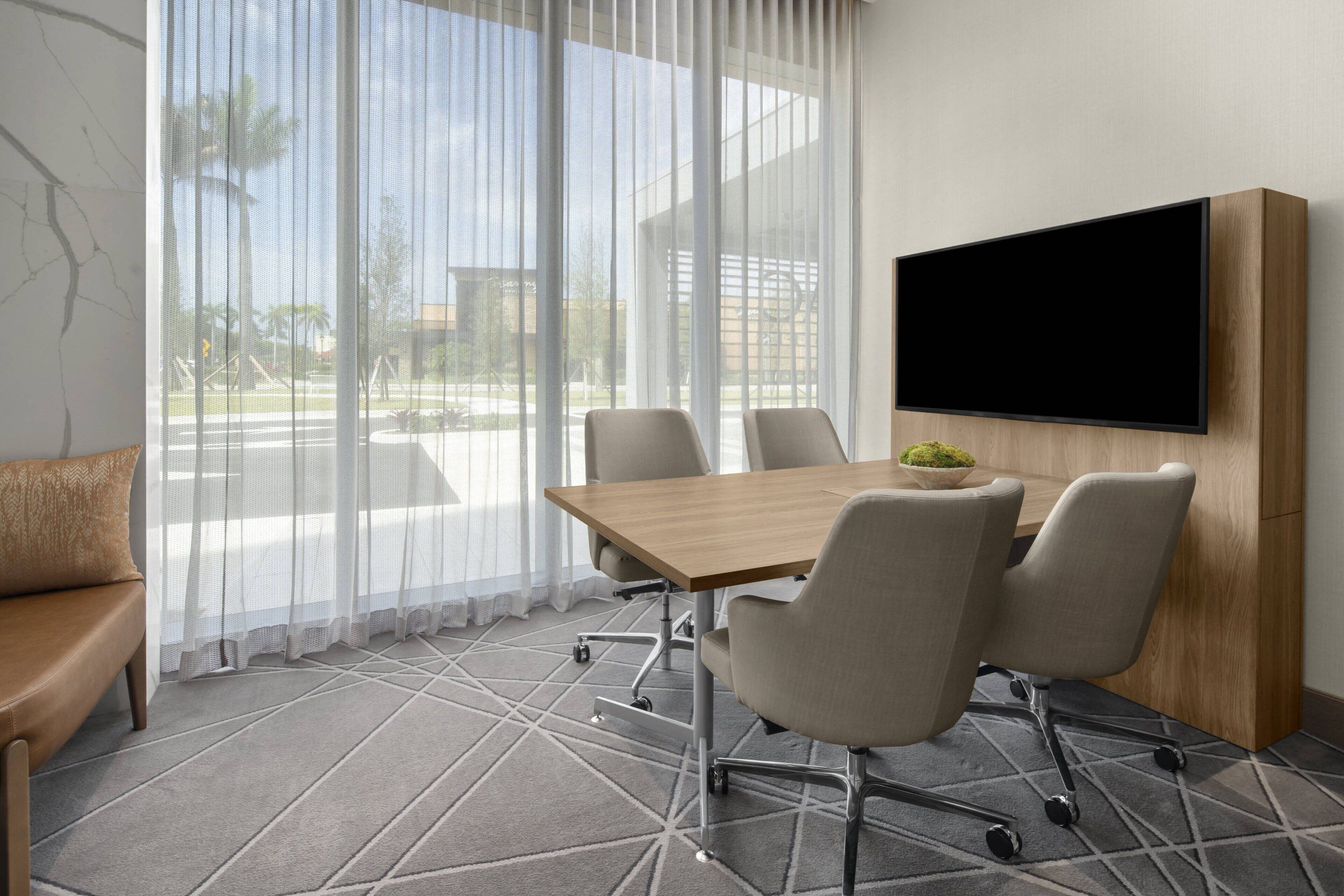 Un salón de conferencias con una mesa grande, cuatro sillas, un televisor montado en la pared y un sofá.
