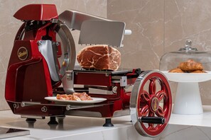 A red meat slicer with a plate of sliced meat and a glass dome containing pastries. - AC Hotel Fort Lauderdale Sawgrass Mills / Sunrise (Sunrise)