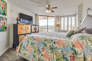 A bedroom with a bed, ceiling fan, TV, and artwork on the walls.
