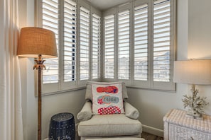 A room with a chair, a lamp, and a window with shutters.