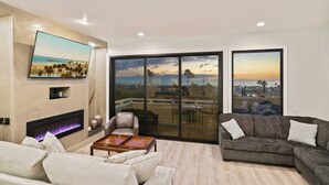 A living room with a fireplace, a sofa, a coffee table, and a TV mounted on the wall. - Newly remodeled home with breathtaking ocean view. (Newport Beach)