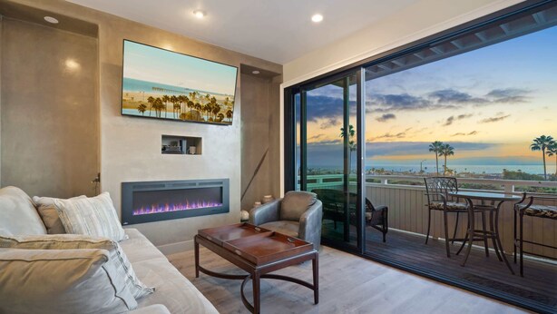 A modern living room with a fireplace, a sofa, and a view of the ocean through large sliding doors. - Newly remodeled home with breathtaking ocean view. (Newport Beach)