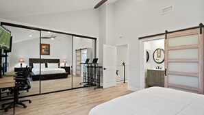 A modern bedroom with a large bed, a desk with a chair, a sliding door, and a television. - Newly remodeled home with breathtaking ocean view. (Newport Beach)