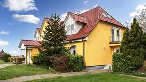 Uma casa amarela com telhado vermelho, rodeada por relva verde e árvores.