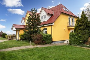 Ein gelbes Haus mit rotem Dach, umgeben von grünem Gras und Bäumen.