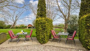 An outdoor patio with a table and chairs, surrounded by neatly trimmed hedges and trees.