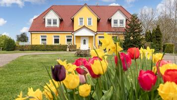 A yellow house with a red roof, surrounded by a well-maintained lawn and colorful tulips.