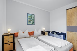 Ein Schlafzimmer mit zwei Betten, einem Nachttisch mit Schubladen, einer Lampe und einem gerahmten Bild an der Wand.