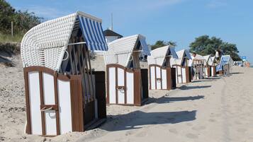 A row of beach huts with striped awnings, arranged along a sandy beach.