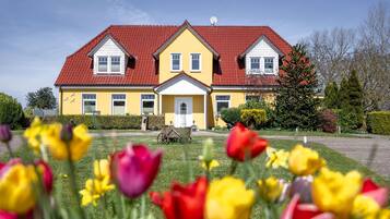 A yellow building with a red roof and white trim, surrounded by a well-maintained lawn and colorful tulips.