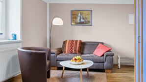 A living room with a brown leather sofa, a round coffee table with fruit, a floor lamp, and a sailboat painting on the wall.