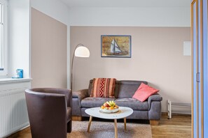 Ein Wohnzimmer mit einem braunen Ledersofa, einem runden Couchtisch mit Obst, einer Stehlampe und einem Segelbootgemälde an der Wand.