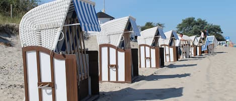 A row of beach huts with striped awnings, arranged along a sandy beach.
