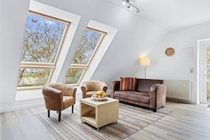 Un salon moderne avec un plafond de style industriel, de grandes fenêtres, un canapé en cuir marron, une table basse et une lampe.