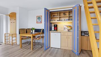 A compact kitchen with a dining area, wooden cabinets, a coffee maker, and a small refrigerator.