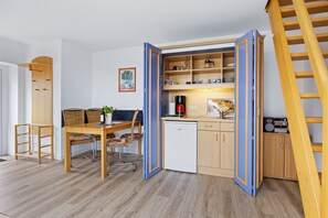 Eine kleine Küche mit Essecke, Holzausstattung, einer Kaffeemaschine und einem kleinen Kühlschrank.