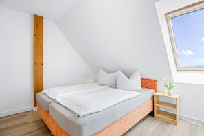 Une chambre moderne avec un plafond en pente, un lit avec une literie grise, une petite table de chevet en bois et une fenêtre donnant sur le ciel.