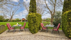 Une terrasse extérieure avec une table et des chaises, entourée de haies et d’arbres soigneusement taillés.