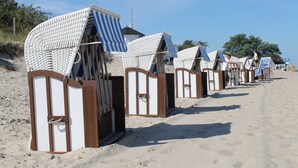 Eine Reihe von Strandhäusern mit Streifenmarkisen, die entlang eines Sandstrandes angeordnet sind.