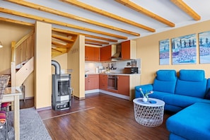 Eine moderne Küche mit Holzbalken, orangefarbenen Schränken und einem blauen Sofa in einem Wohnbereich.