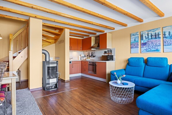 Een moderne keuken met houten balken, oranje kastjes en een blauwe bank in een woonruimte.