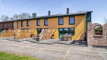 A yellow building with a brick section, outdoor seating, and a wooden deck.