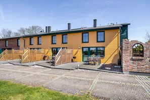 Ein gelbes Gebäude mit Backsteinelementen, Außenbereich und einer Holzterrasse.
