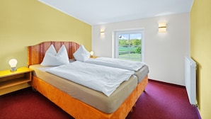 Ein Schlafzimmer mit Bett, Nachttischen, einem Fenster und Blick auf eine grüne Landschaft.