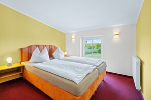 Ein Schlafzimmer mit Bett, Nachttischen, einem Fenster und Blick auf eine grüne Landschaft.