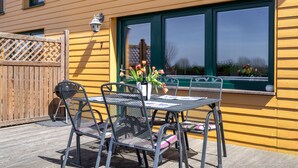 Eine Terrasse mit Tisch und Stühlen, ein Holzzaun und ein Fenster mit grüner Rahmenverkleidung.