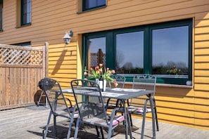 Een terras met een tafel en stoelen, een houten omheining en een raam met groene sierlijsten.