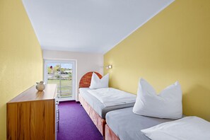 Ein Hotelzimmer mit zwei Einzelbetten, einem Holztisch und einem violetten Teppich.