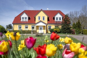 Een geel gebouw met een rood dak en witte details, omringd door een verzorgd gazon en kleurrijke tulpen.