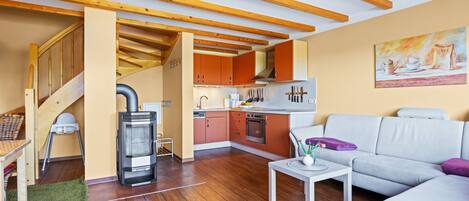 A modern kitchen with wooden beams, a dining area with a white table, and a living room with a grey sofa.