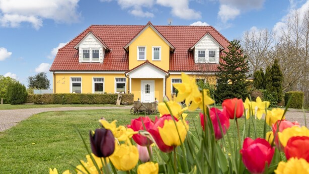 A yellow house with a red roof, surrounded by a well-maintained lawn and colorful tulips.