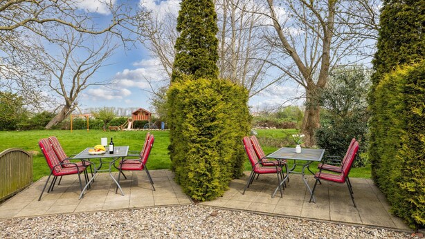 Patio esterno con tavolo e sedie, circondato da siepi curate e alberi.