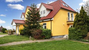 Une maison jaune avec un toit rouge, entourée d’herbe verte et d’arbres.