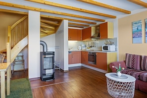 A compact kitchen with modern appliances, a dining area with a wooden table, and a cozy seating area with a patterned sofa.