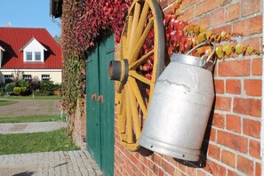 A metal bucket mounted on a brick wall, a wooden wheel, and a green door with ivy.