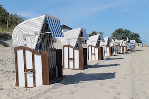 Eine Reihe von Strandhäusern mit Streifenmarkisen, die entlang eines Sandstrandes angeordnet sind.