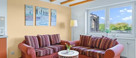 Un salon chaleureux avec deux canapés, une table basse ronde et une fenêtre donnant sur un immeuble et des arbres.