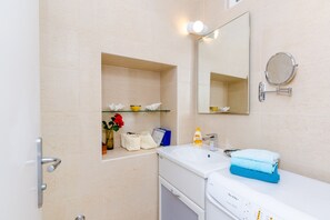A bathroom with a white sink, a mirror, a shelf with toiletries, and a towel rack. - Apartment Domino 18 (Dubrovnik)
