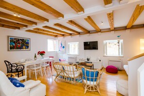 A spacious living area with wooden beams, a dining table with chairs, a sofa, a TV, and a window with a view. - Apartment Domino 18 (Dubrovnik)